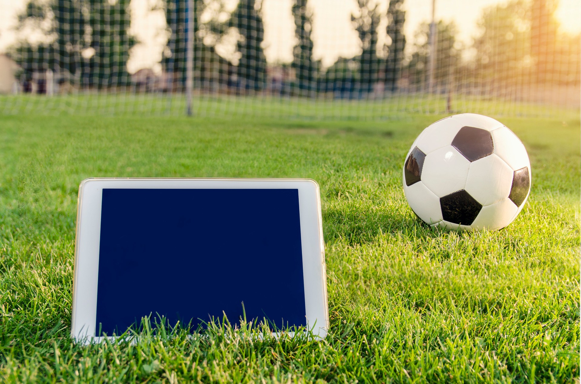 White tablet on grass field next to soccer ball